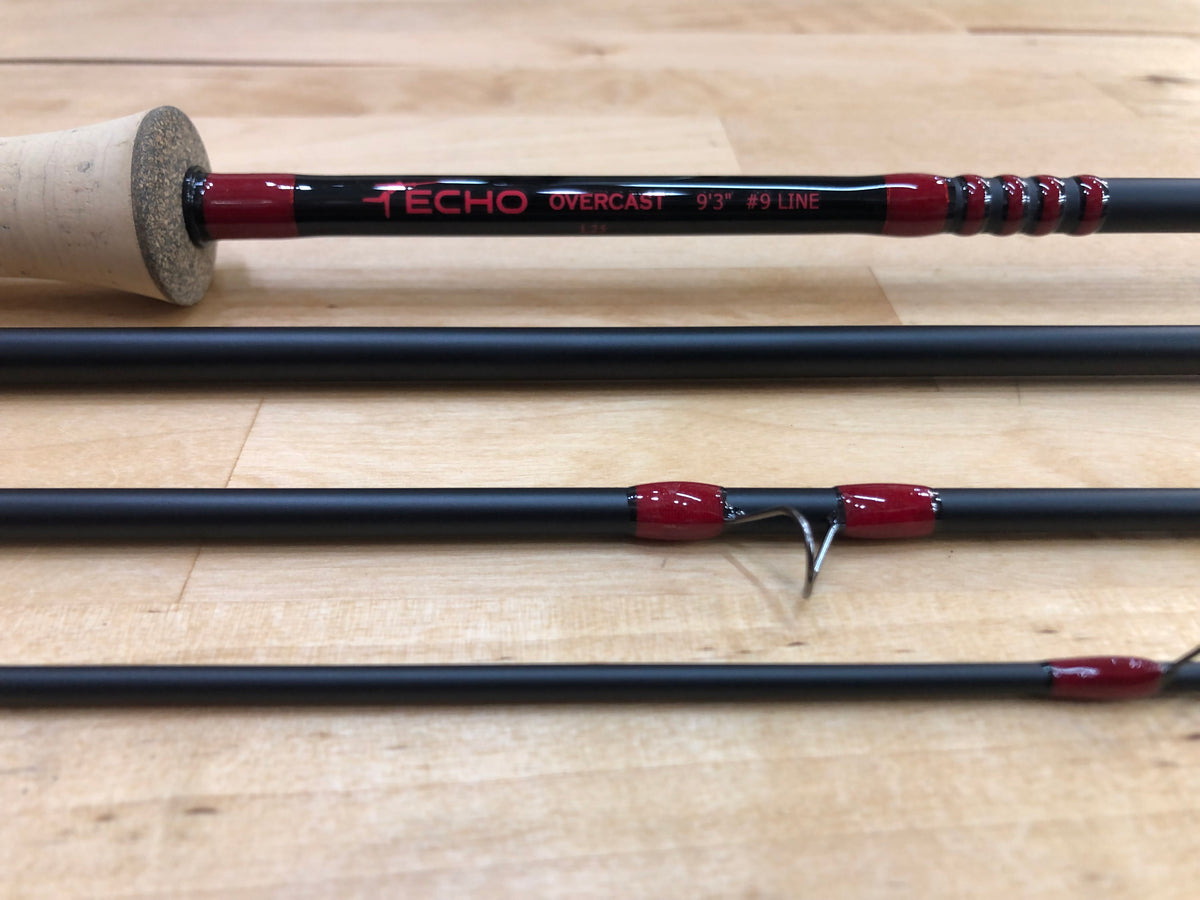 A split black fishing rod with red accents and a cork-wrapped handle, shown on a light wood surface. The brand name 'TECHO' is printed on the rod.